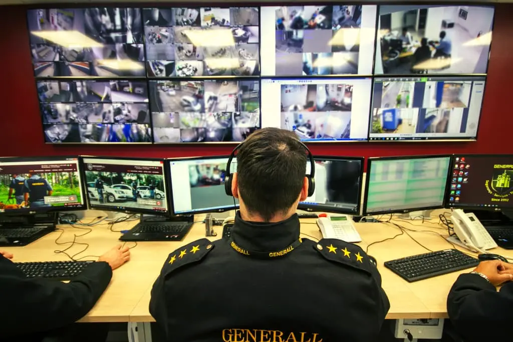 homem de costas sentado em frente a telas de uma central de monitoramento