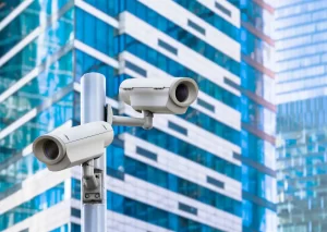Câmeras de segurança em via urbana com edifícios modernos ao fundo, ilustrando videomonitoramento para proteção perimetral.